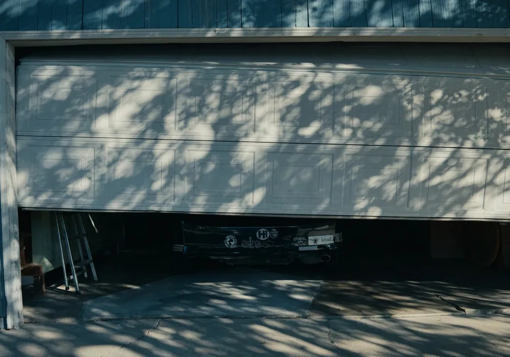 White sectional garage door jammed partway open, blocking the car inside